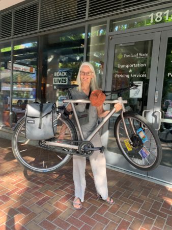 A woman holds a silver ebike aloft in front of her torso by the chainstay and downtube