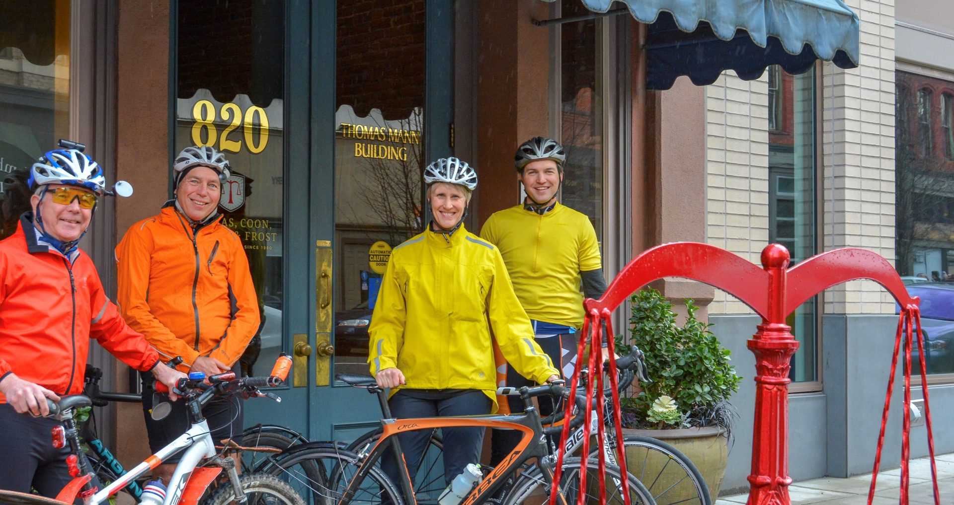 Four people in brighlty colored jackets stand with bicycles in fornt of law office.
