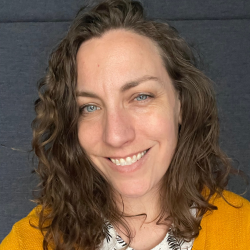 Smiling woman with brown curly hair and yellow sweater